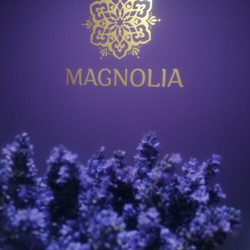 Das Logo von Magnolia in Gold auf lila Wand und ein Strauß Lavendel